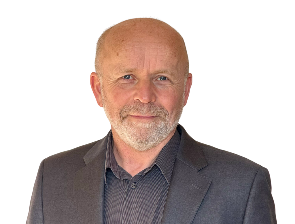 Image shows a man in a dark suit and shirt smiling towards the camera.